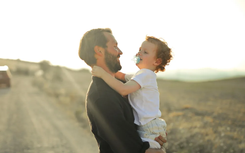 A father holding his smiling young child outdoors at golden hour